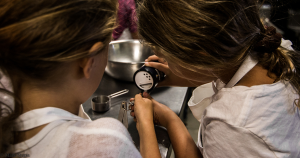 Two girls pour salt to a measuring spoon